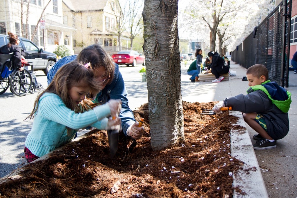 (Photo by Daniella Rascón) Virginia Mojica (center) and grandchildren Genesis and Gabriel Medina work on new planters outside the John F. Kennedy School in Hyde Square during the Boston Shines cleanup April 27. Students, staff and parents built the boxes earlier this year with a grant from Lowe’s.