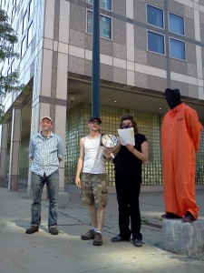 (Gazette Photo by John Ruch) Kinetic Theorist of MassOps (second from right) speaks at the June 1 protest outside police headquarters while joined by (from left) Alex Marthews of Digital Fourth, Garret Kirkland of Defend the Fourth and a protester in prison garb.