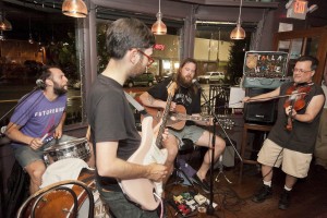 Gordon Gano (far right), former singer and violinist for the 1980s hit band Violent Femmes, plays with local band Tallahassee in a surprise appearance at a June 24 JP Music Festival fund-raiser at the Tres Gatos bookstore/restaurant at 470 Centre St. Gano, whose sister lives in JP, performed at the debut local music fest in 2011. This year’s edition is slated for Sept. 7 at Jamaica Pond Park. See jpmusicfestival.com. (Photo by Tony Sahadeo)